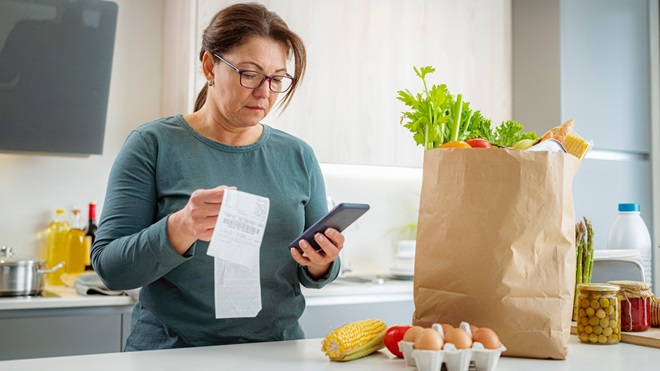 woman standing in the kitchen looking at a supermarket receipt